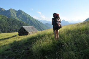 Une femme en randonnées dans une prairie près d'une cabane au pied des montagnes